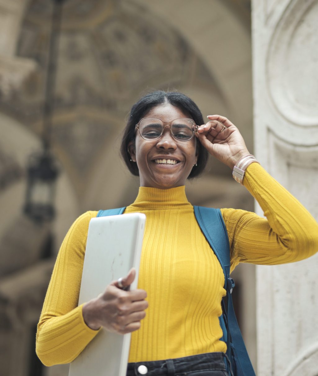 young woman at the entrance of a school holding a computer