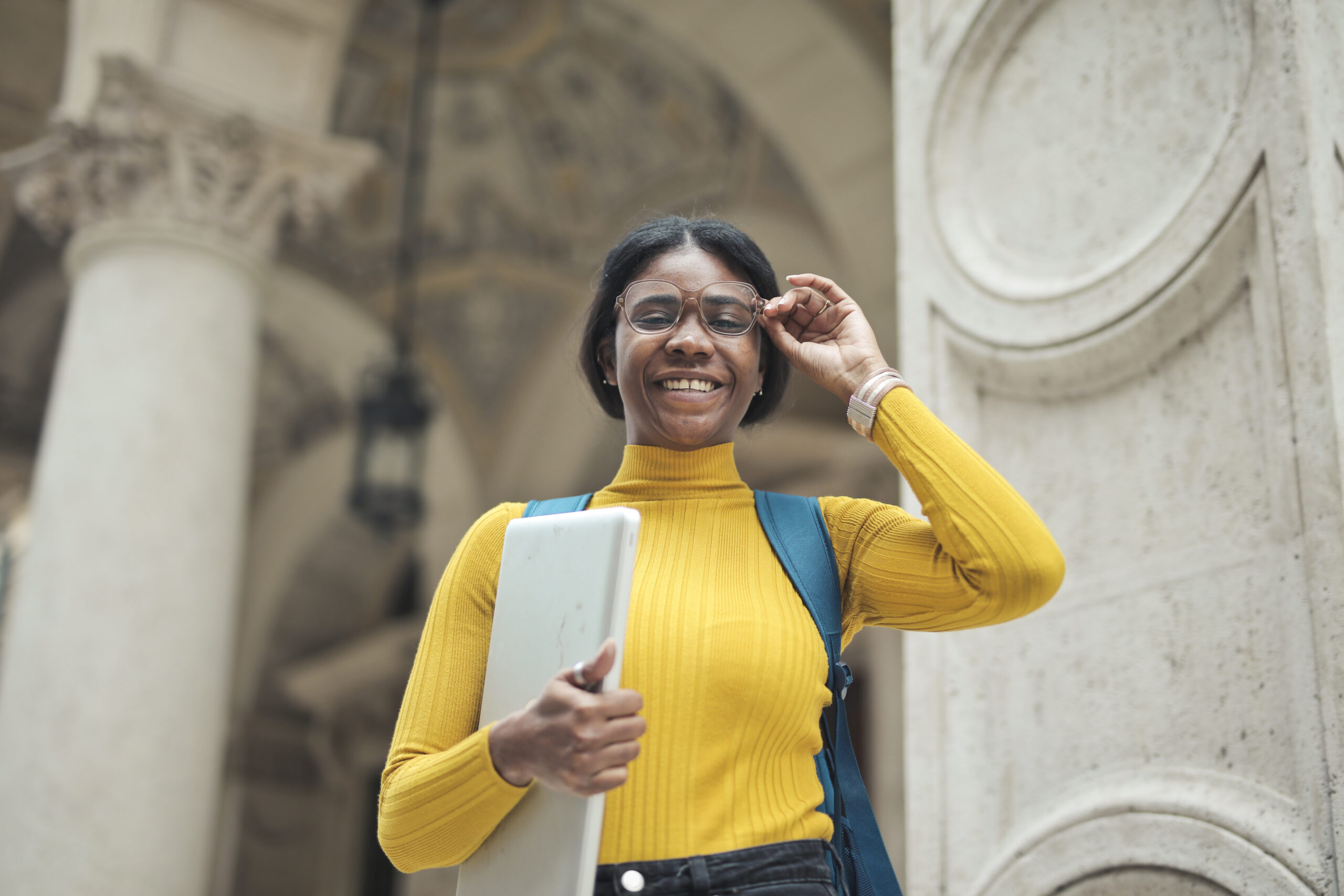 young woman at the entrance of a school holding a computer